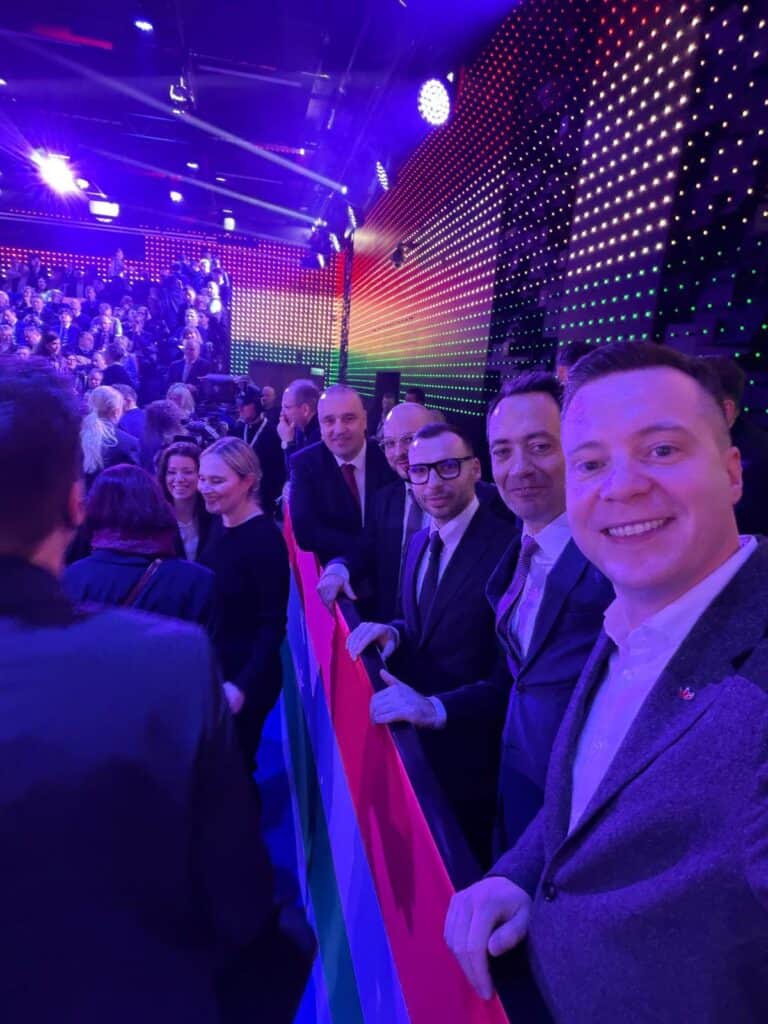 Es politikusok Orbán évértékelőjén, a háttérben színes fények és tömeg látható.