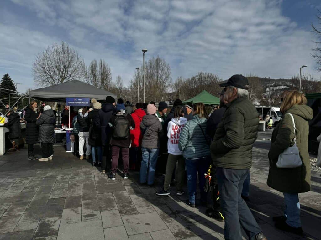 Emberek sorban állnak egy kampányeseményen a Tiszánál, hideg időben.