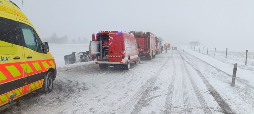 Állami mentőautó és tűzoltó járművek a hóval borított úton, közlekedési káosz és útlezárások miatt.